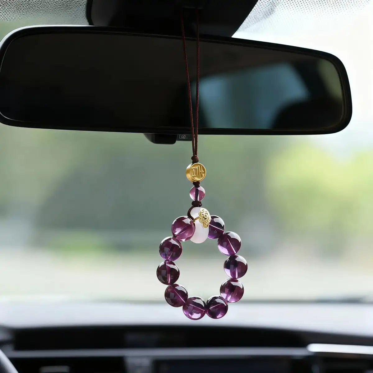 The amethyst beaded charm hanging from a car's rearview mirror with a blurred background.