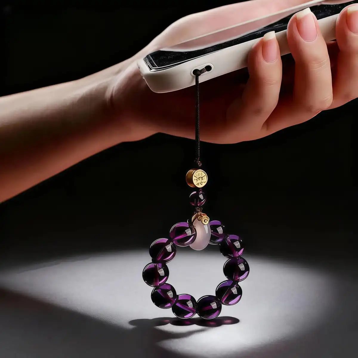 A hand holding a white smartphone with the purple amethyst charm attached as a phone strap.