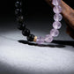 A vertical close-up shot of the Dual Energy Bracelet using dramatic lighting. The light shines through the translucent amethyst beads, contrasting with the solid black obsidian, symbolizing the balance of clarity and deep peace.