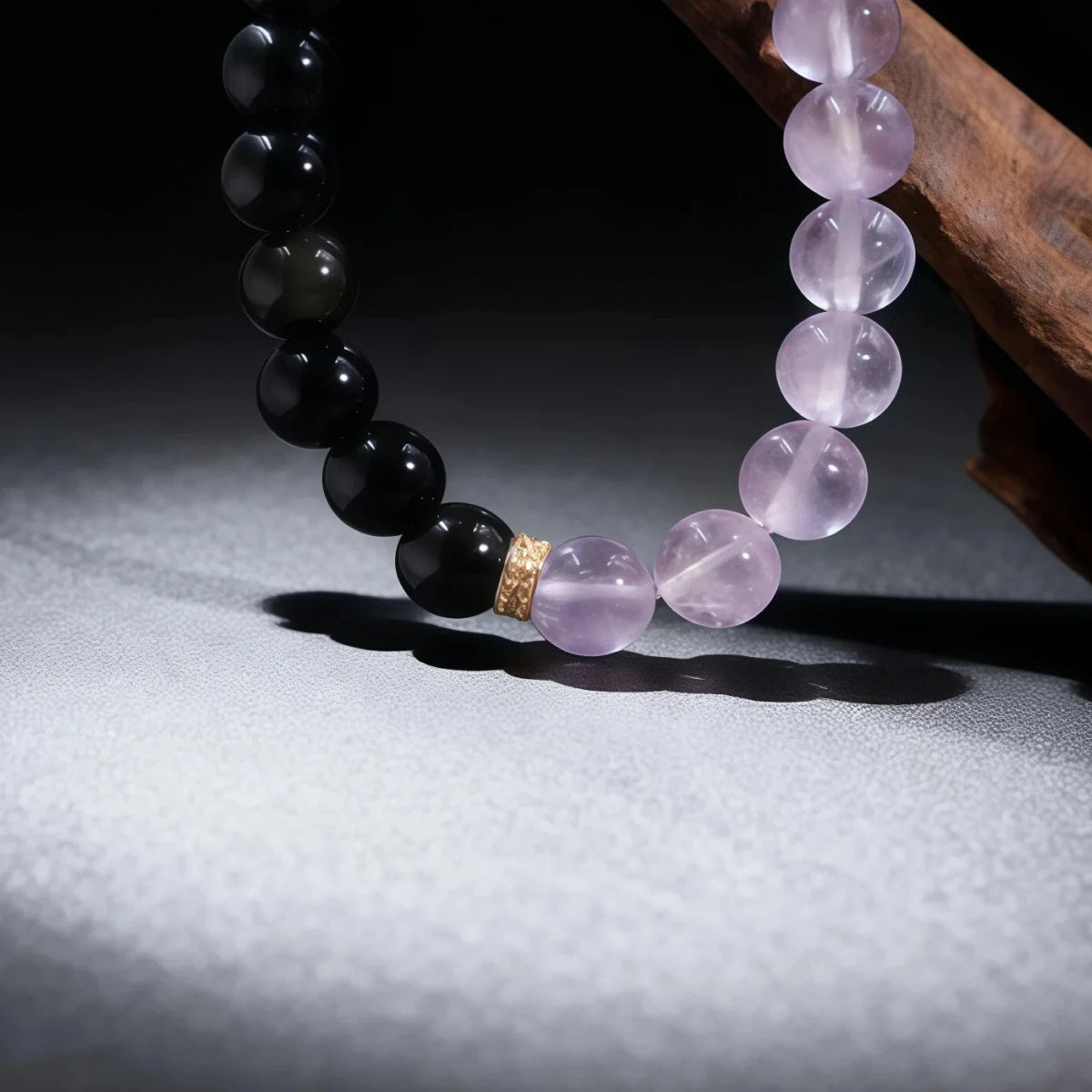 A vertical close-up shot of the Dual Energy Bracelet using dramatic lighting. The light shines through the translucent amethyst beads, contrasting with the solid black obsidian, symbolizing the balance of clarity and deep peace.