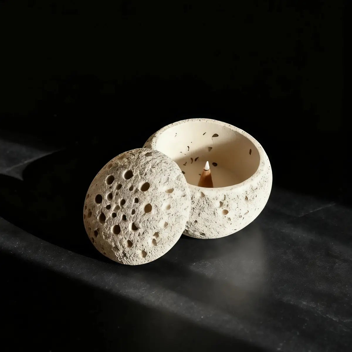 Ceramic incense burner with a lit candle on a dark surface