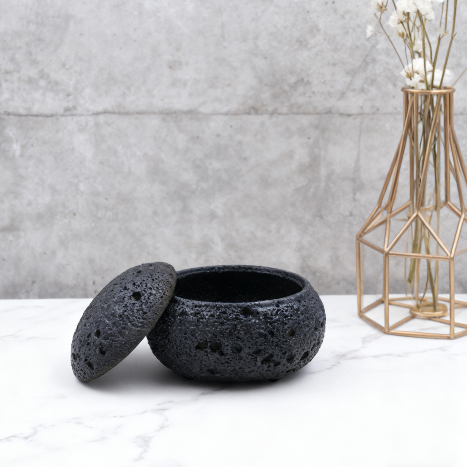 Black textured pot with lid on a marble surface with a geometric vase in the background.
