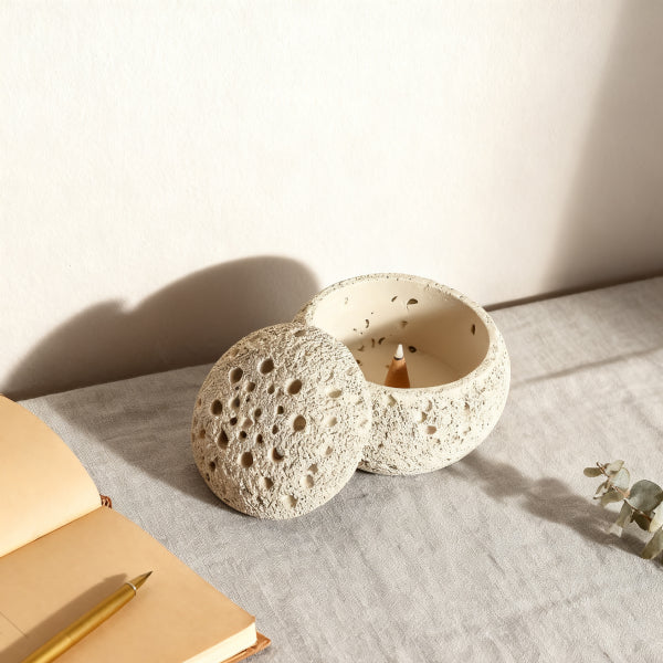 Textured ceramic candle holder with a small candle inside on a light surface.