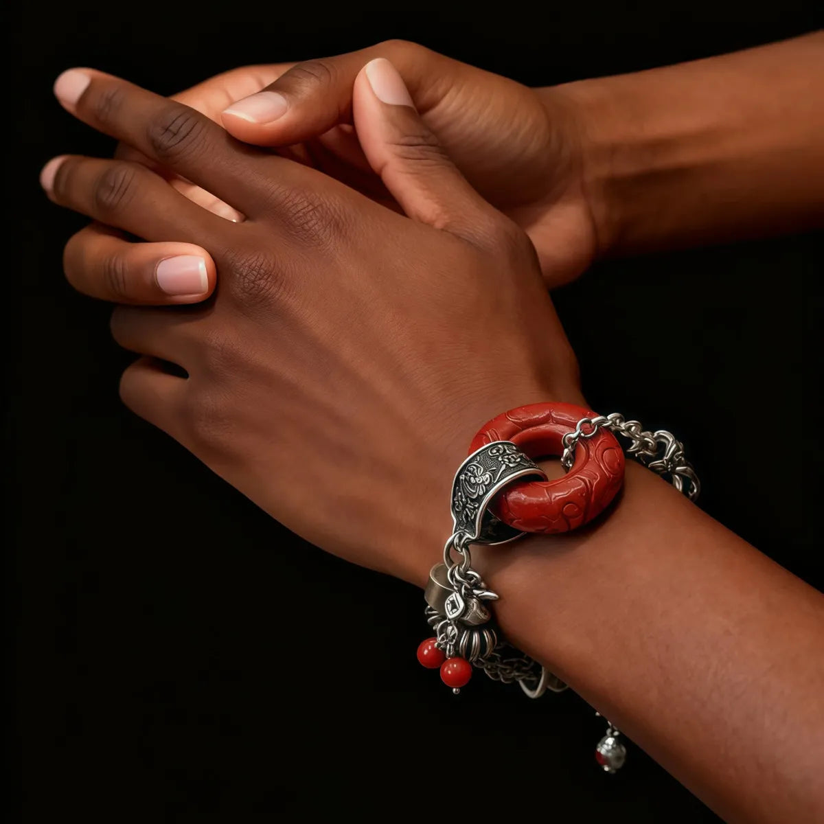 Close-up of a wrist wearing a red and tibetan silver bracelet against a black background