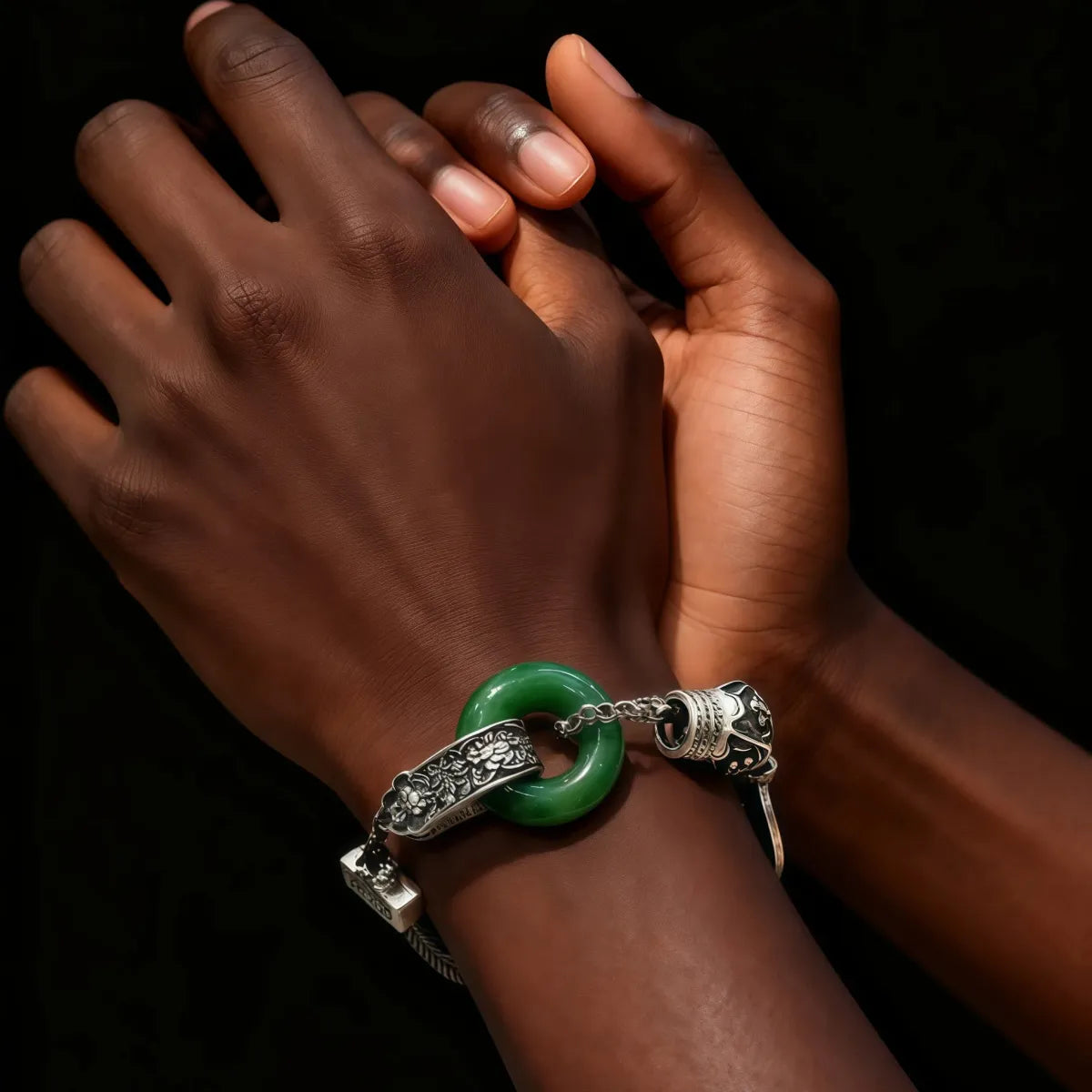 Close-up of a hand wearing a tibetan silver bracelet with a green stone on a dark background