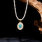 Balance Grace Tibetan Harmony Pearl Necklace featuring a strand of white pearls and a gold oval pendant with a central turquoise stone surrounded by a crystal halo on a mother-of-pearl background.