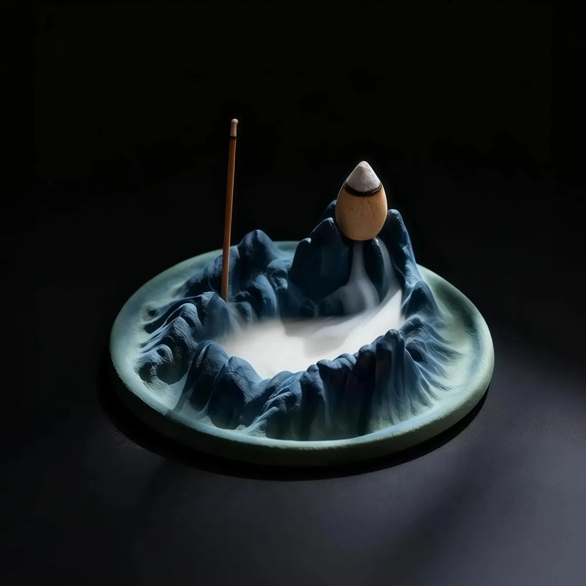 Ceramic incense burner shaped like a mountain with two incense sticks on a dark background