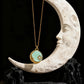 Necklace with a turquoise pendant hanging from a crescent moon sculpture on a dark background