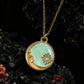 Gold necklace with a green pendant featuring a face and sun design on a dark background.