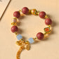 Bracelet with red beads, gold accents, and colorful charm on a beige background