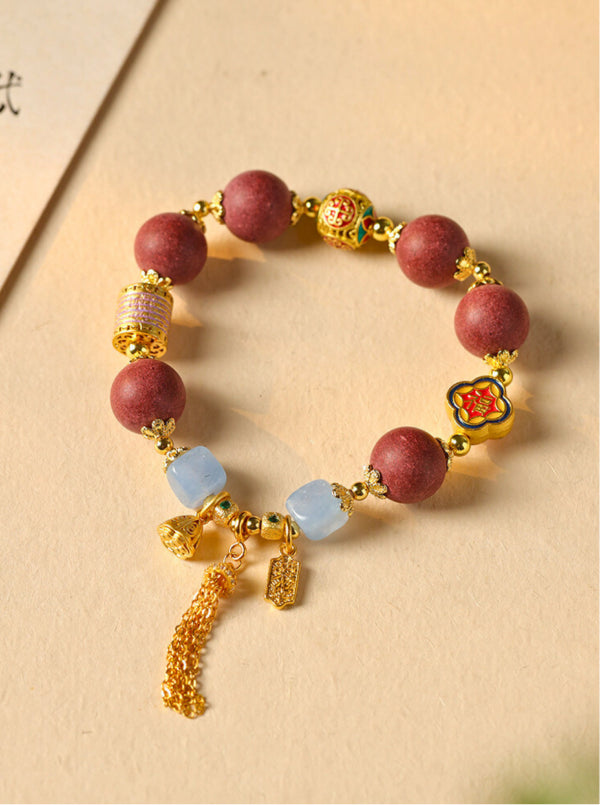 Bracelet with red beads, gold accents, and colorful charm on a beige background