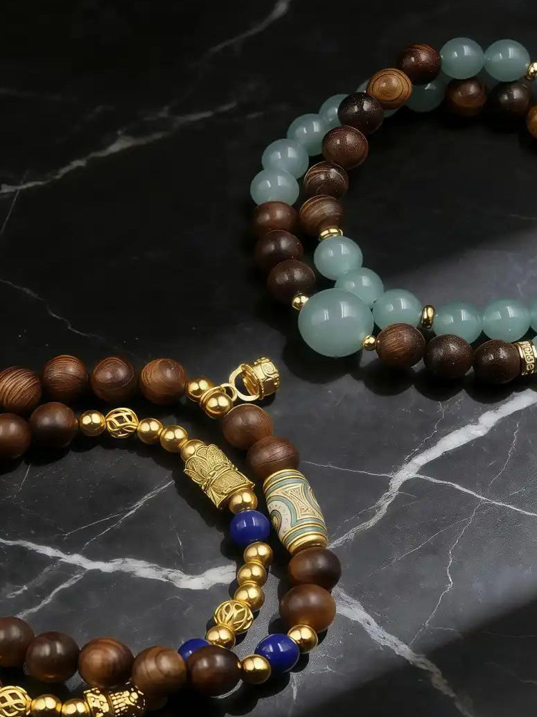 Two beaded bracelets with gold accents on a dark marble surface
