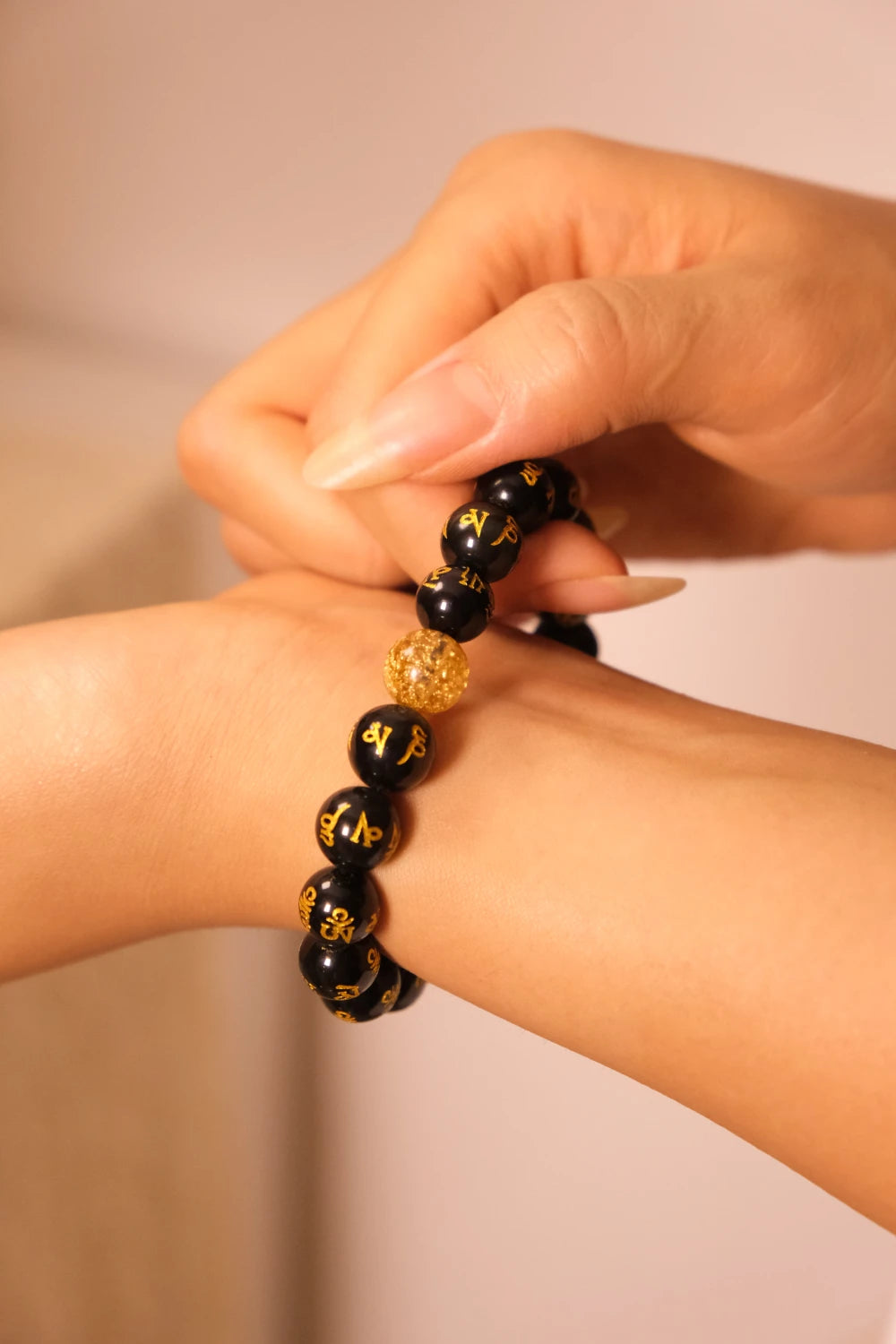 Black beaded Buddhist Mantra bracelet with gold accents on a wrist against a neutral background
