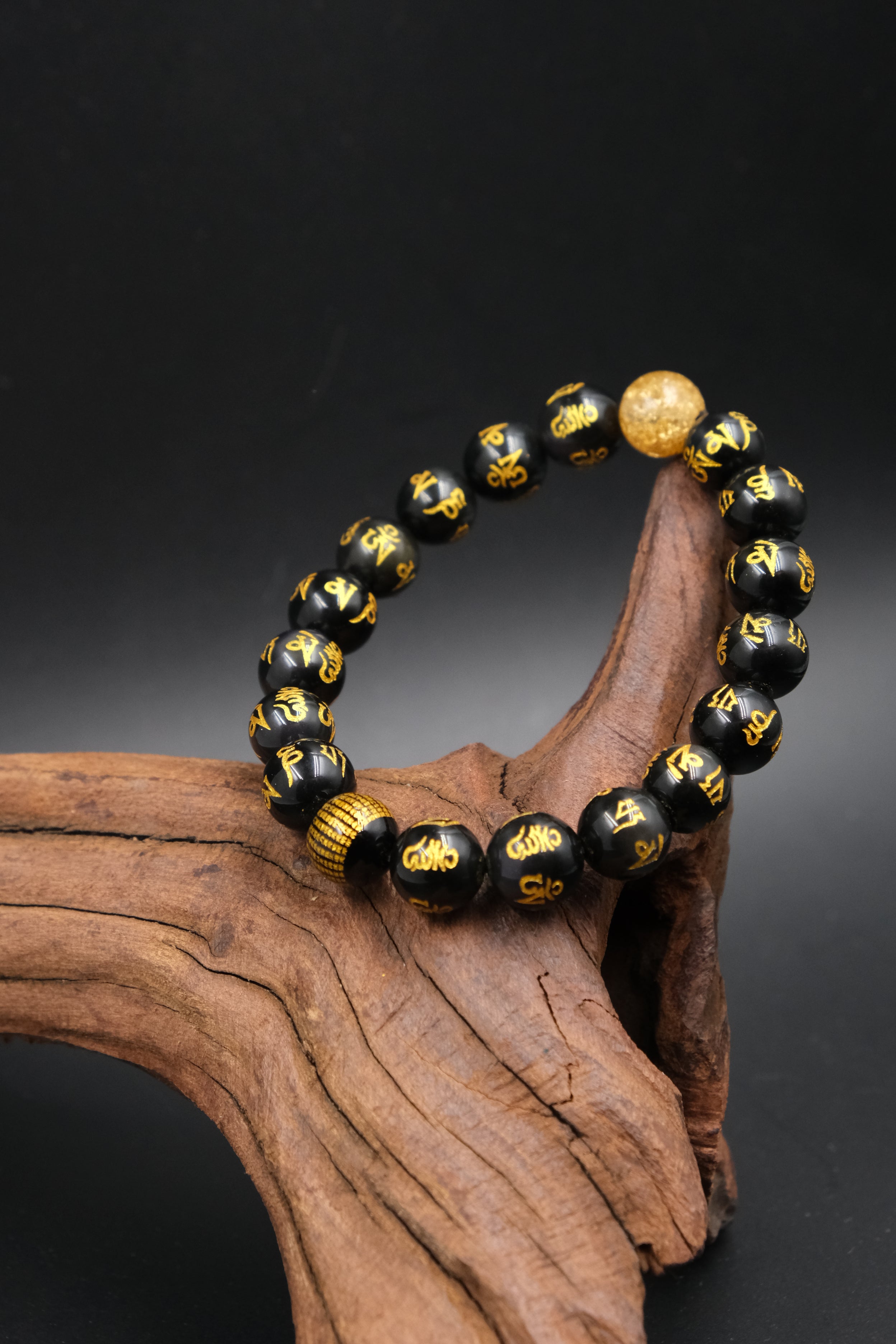 Black and gold Buddhist Mantra beaded bracelet on a wooden surface with a dark background