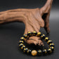 Black and gold Buddhist Mantra  beaded bracelet on a dark surface with wooden driftwood.