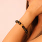 Close-up of a person wearing a black and gold Buddhist Mantra beaded bracelet on a plain background