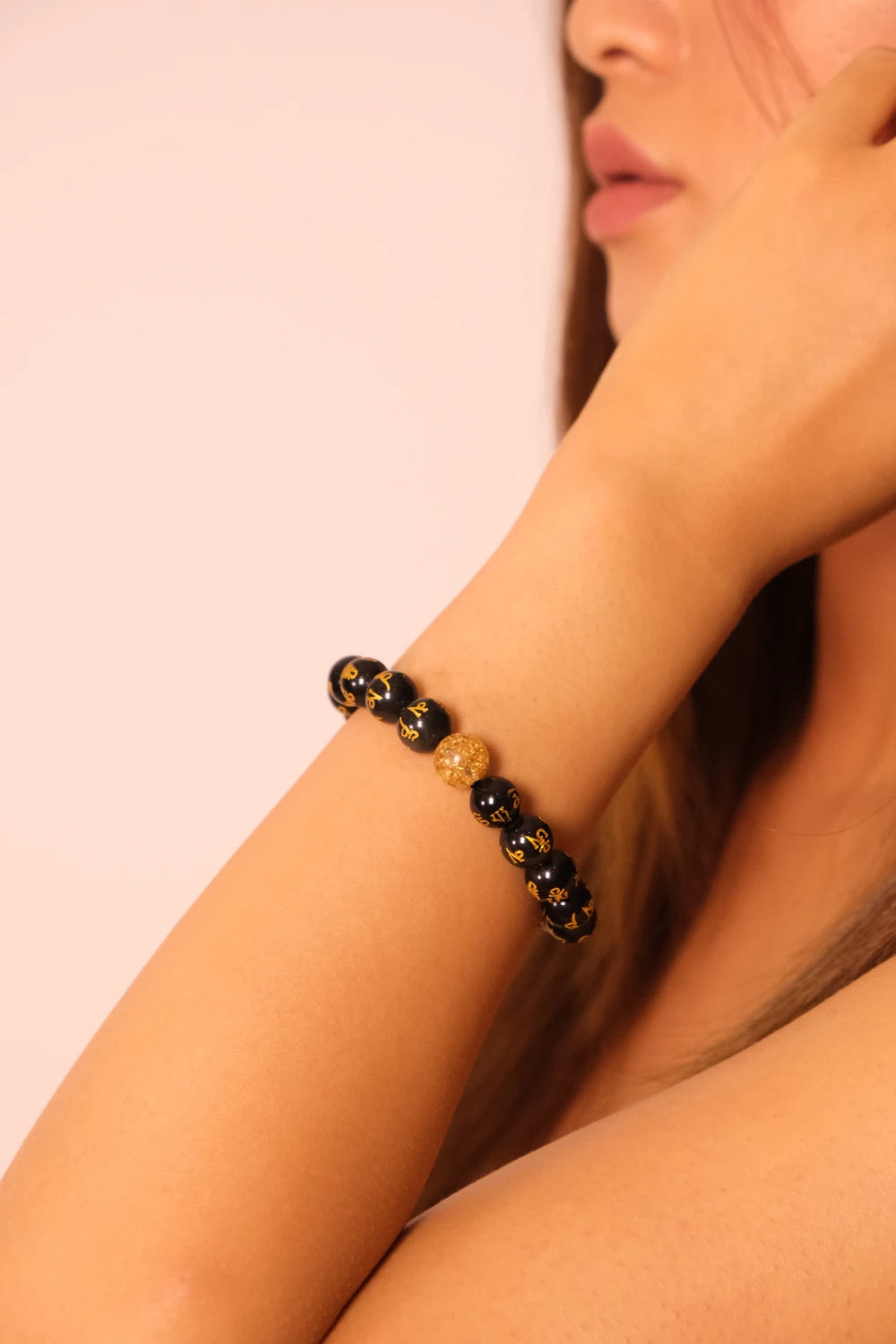 Close-up of a person wearing a black and gold Buddhist Mantra beaded bracelet on a plain background
