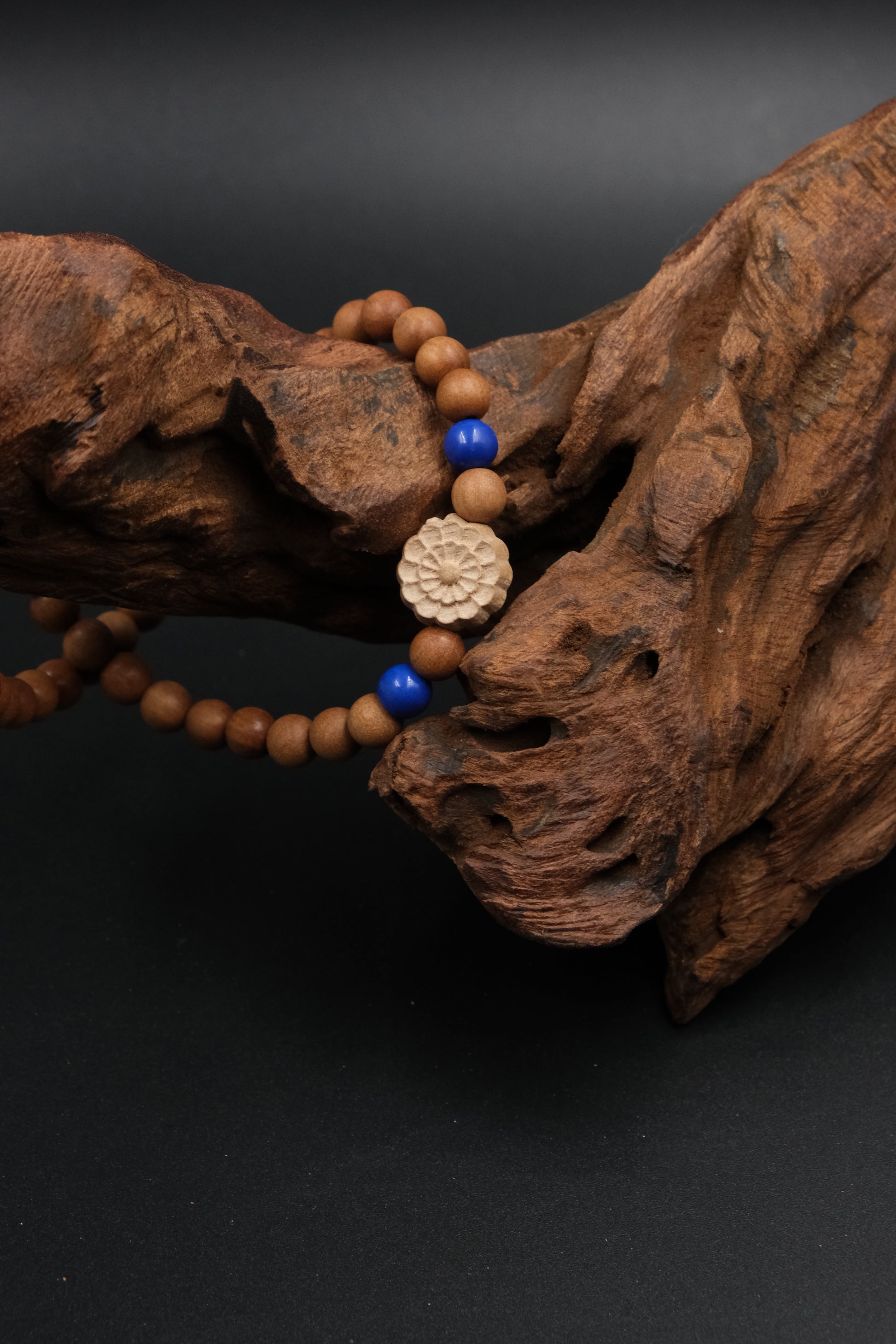 Buddhist Prayer Bracelet with wooden beads and a decorative flower charm on a dark background