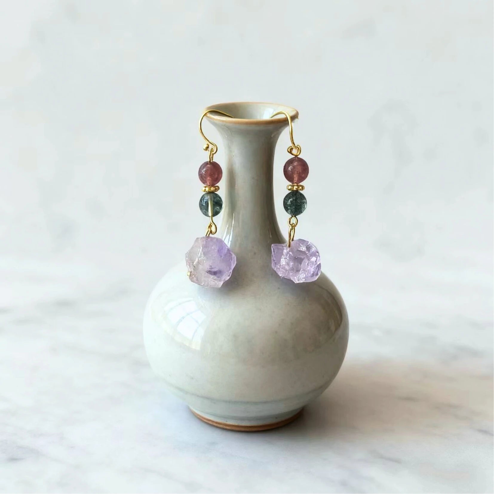 Earrings with colorful beads on a white vase against a light background