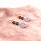 Pair of gold earrings with multicolored beads on a pink surface