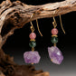 Pair of earrings with purple and green gemstones on a dark background