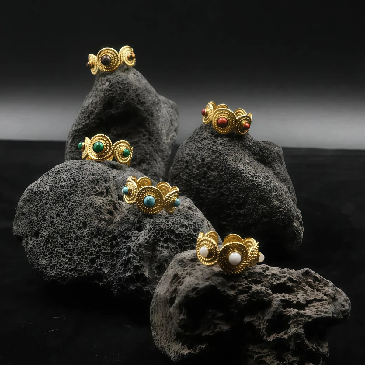 Five different Tibetan Five Elements rings, each featuring a different colored gemstone (pearl, turquoise, agate, etc.) on black volcanic rocks, representing the energy and balance of the Wood, Fire, Earth, Metal, and Water elements.