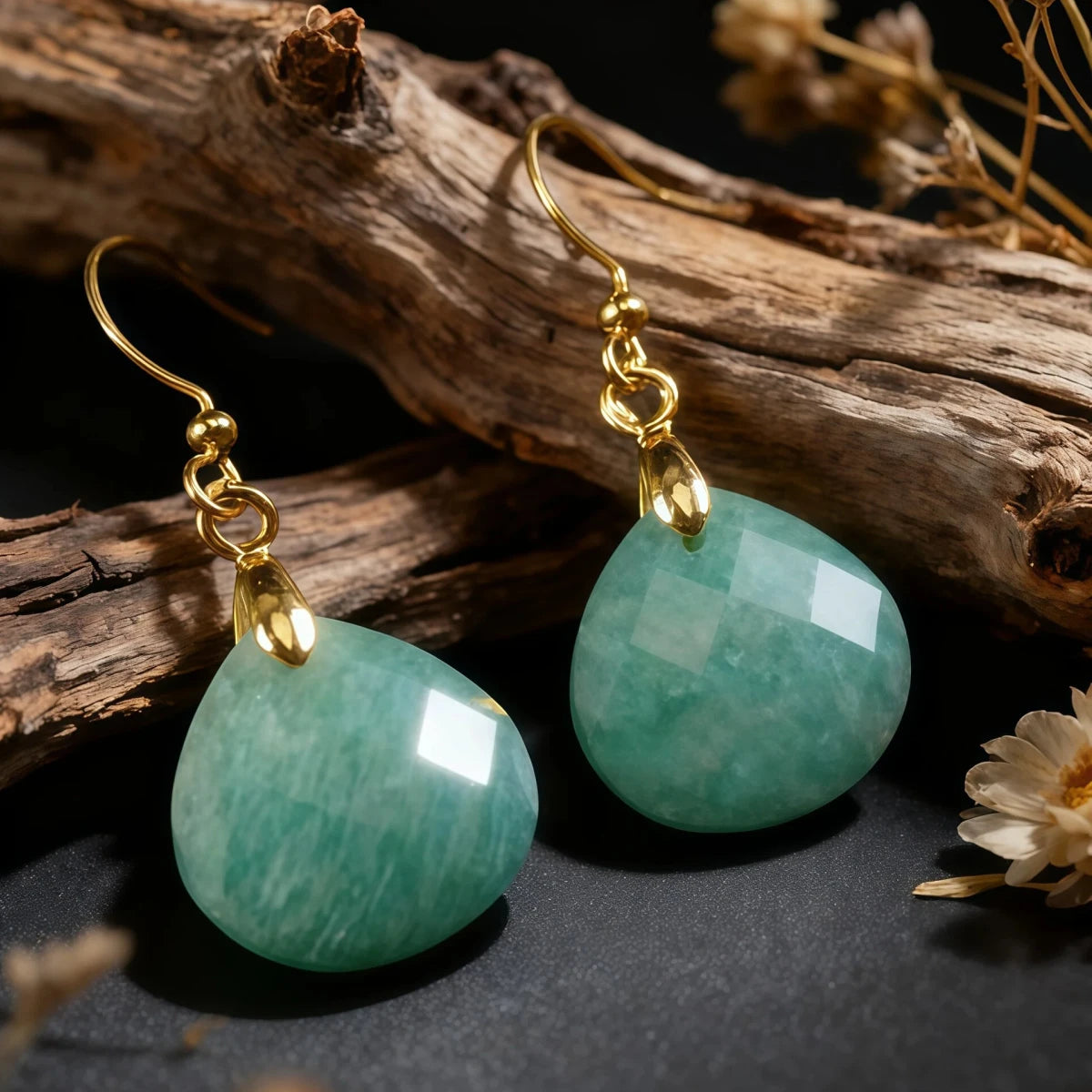 A pair of Tibetan Amazonite earrings resting on a piece of textured driftwood. The natural light highlights the geometric faceting and white inclusions of the green stone, evoking a sense of nature and renewal.