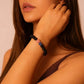 A female model wearing the black bead bracelet with a pink accent stone on her wrist.