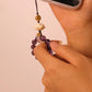 Hand holding a phone with a beaded charm against a plain background,Mindfulness & Protection – Amethyst Prayer Spinner