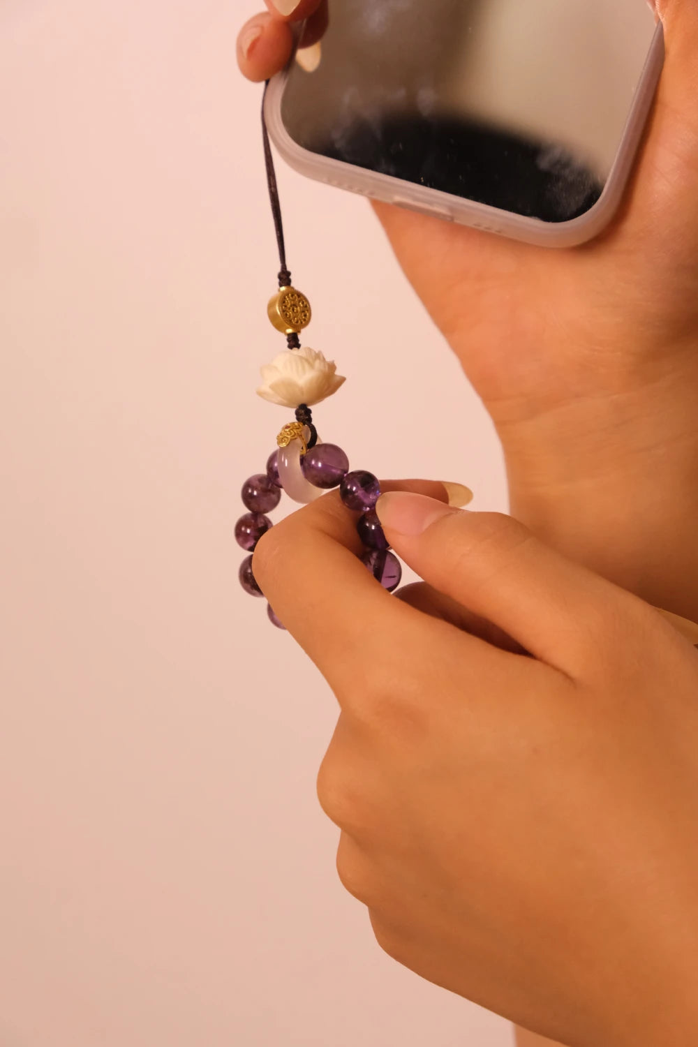 Hand holding a phone with a beaded charm against a plain background,Mindfulness & Protection – Amethyst Prayer Spinner