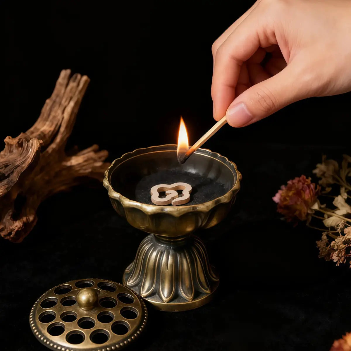 Hand lighting a match over an incense burner with a dark background
