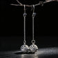 Silver earrings with intricate designs hanging from a branch against a dark background