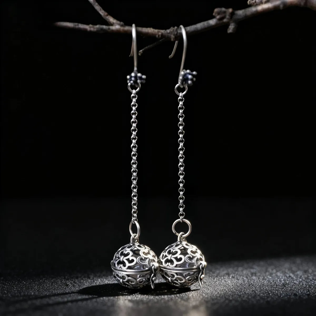 Silver earrings with intricate designs hanging from a branch against a dark background