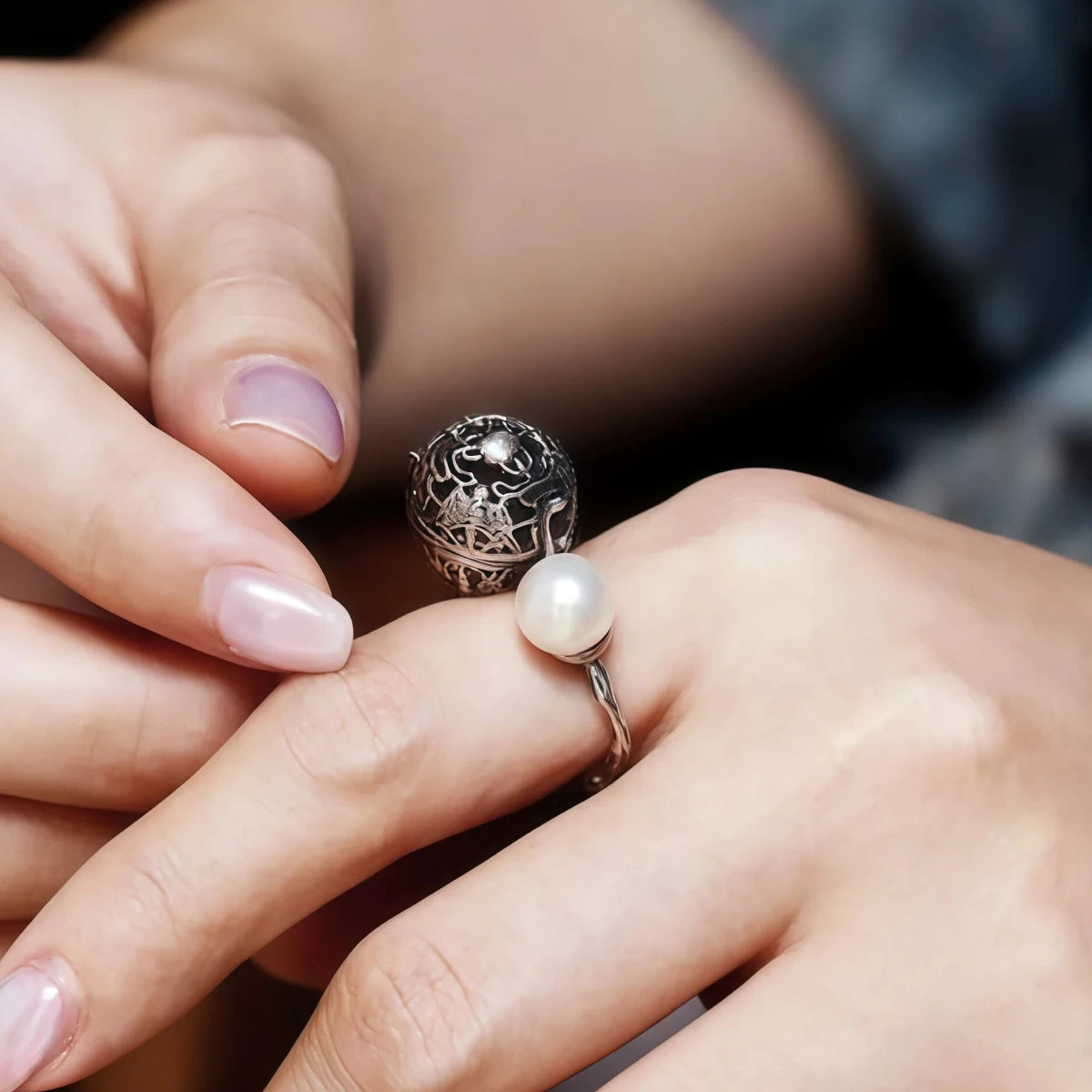 Close-up of a hand wearing a silver ring with a pearl on a blurred background