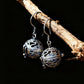 Silver earrings with intricate designs hanging on a branch against a dark background