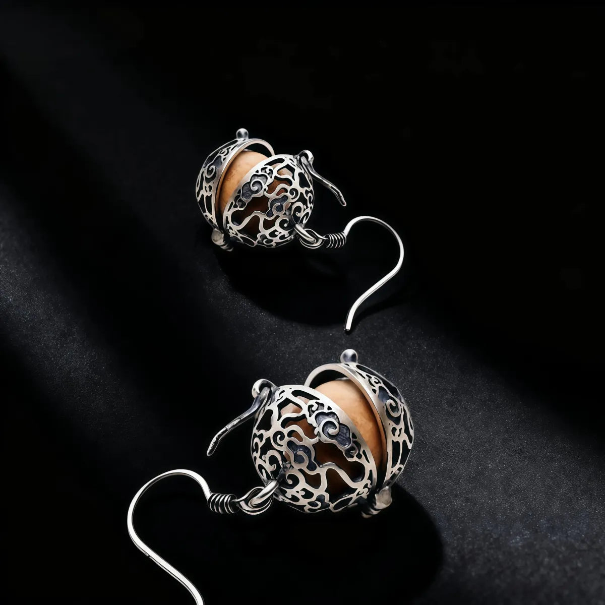 Pair of silver earrings with intricate designs on a black background