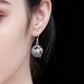 Silver earrings with intricate design worn by a person against a dark background