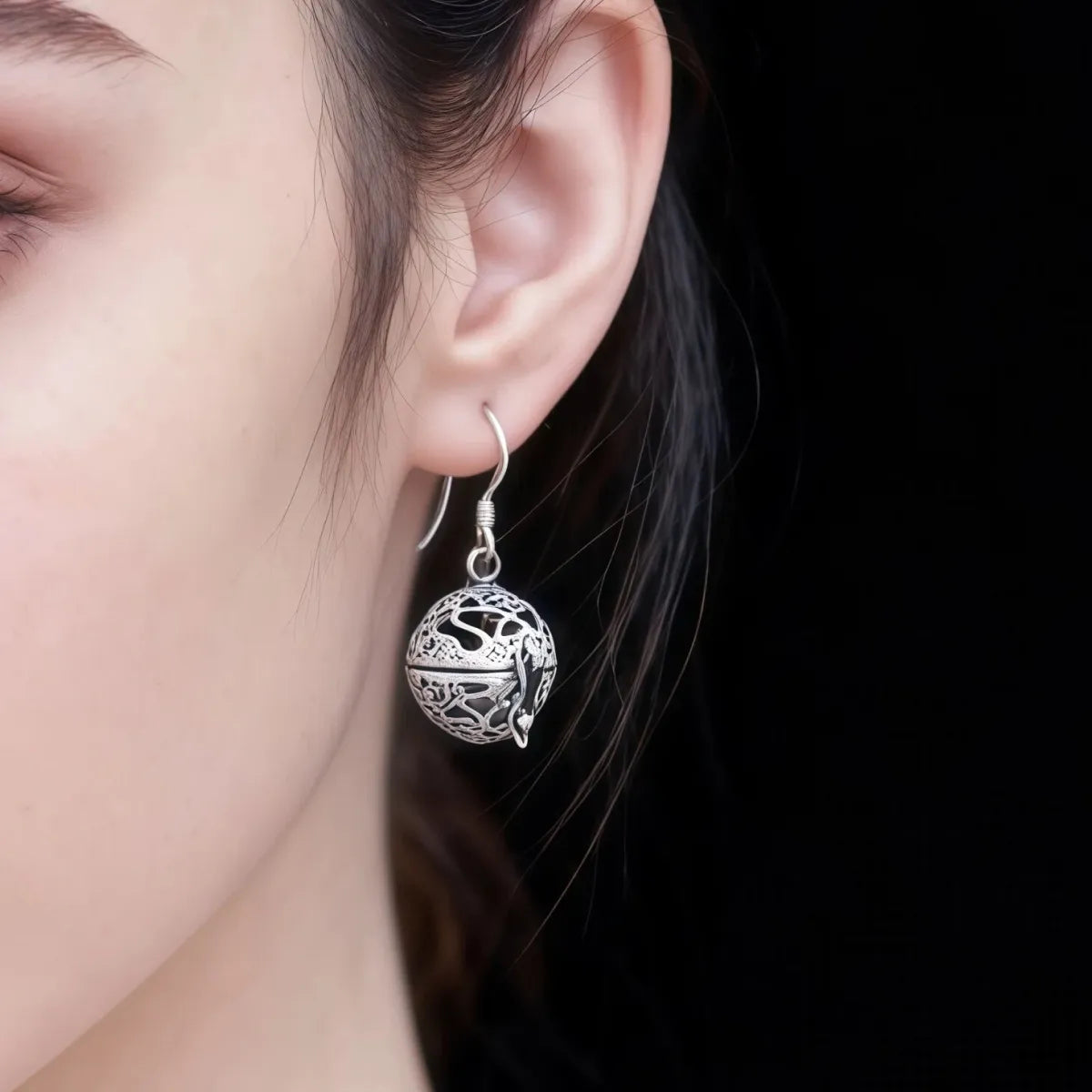 Silver earrings with intricate design worn by a person against a dark background