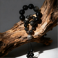 Black beaded bracelet with a silver charm on a wooden branch