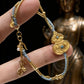 A close-up of the Gourd Bracelet held in hand, with a blurred golden Buddha statue in the background. The image emphasizes the gold hulu charm, turquoise inlay, and delicate tassels, highlighting its spiritual and protective energy.