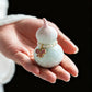 Hand holding a Feng Shui Pearl Gourd Ornament with a pearl bracelet and butterfly charm against a black background