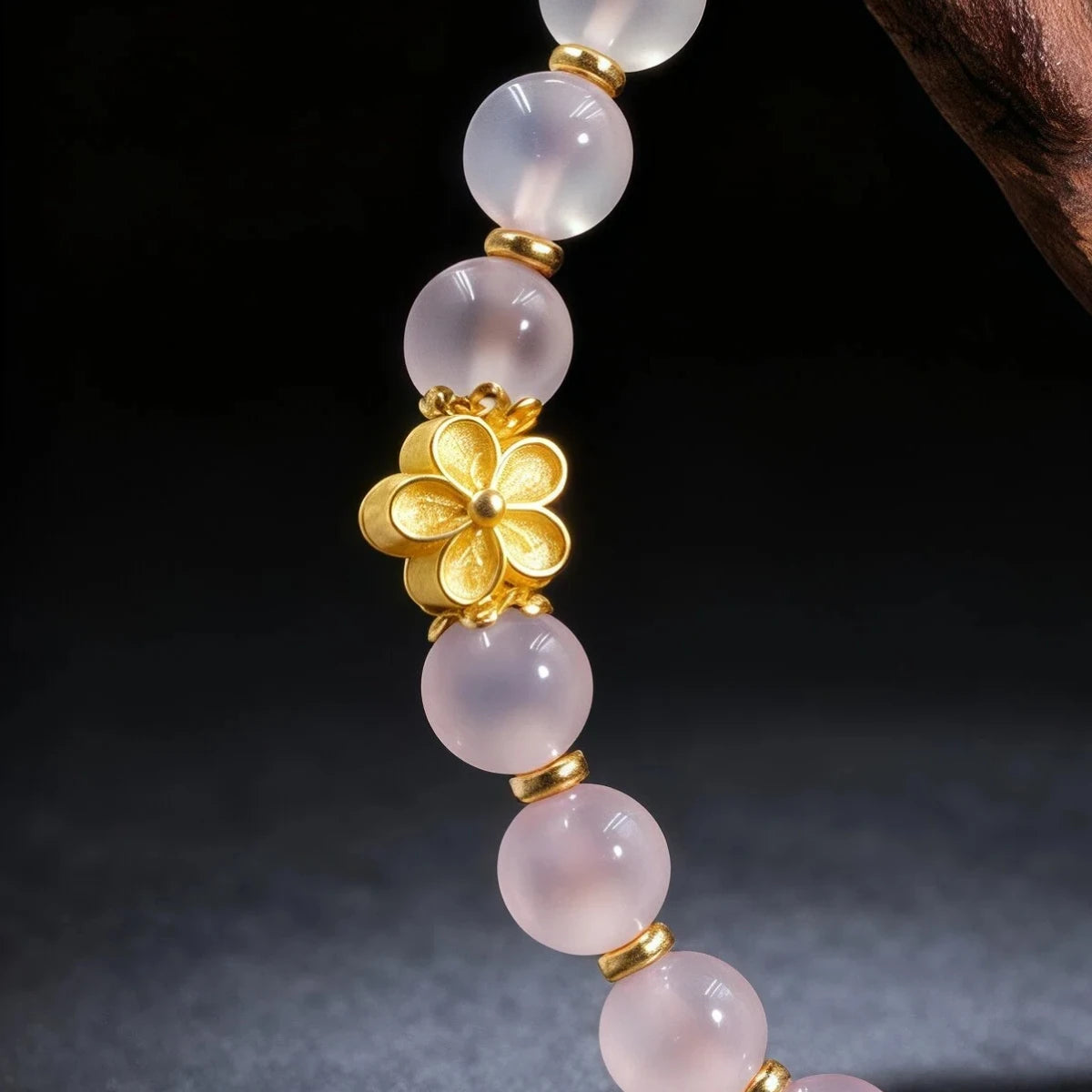 Detail of the bracelet with pink beads and a gold flower pendant on a dark background