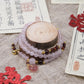 Decorative bracelet with beads on a wooden block, surrounded by red decorative elements and Chinese text.