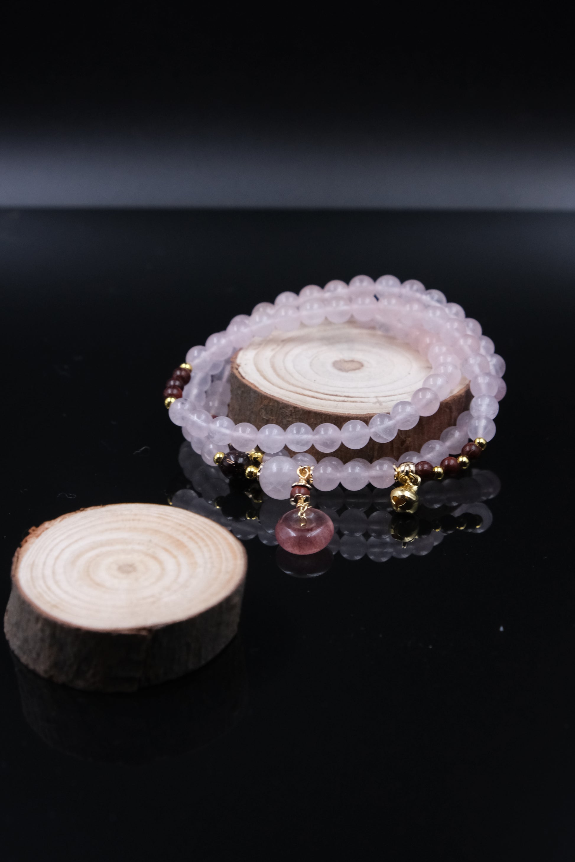 Rose Quartz Amulet Bracelet and a wooden slice on a black background