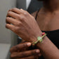 Person wearing a bracelet with a green charm on a neutral background