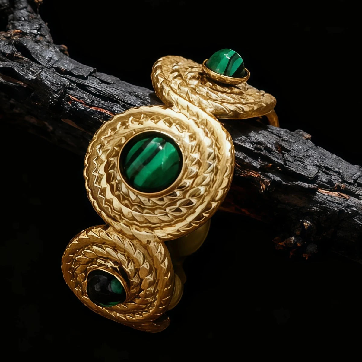 The Tibetan Five Elements Malachite ring draped over a piece of dark, charred wood. The three green Malachite stones connected by gold spiral links emphasize the ring's flexible design and unique Tibetan craftsmanship.