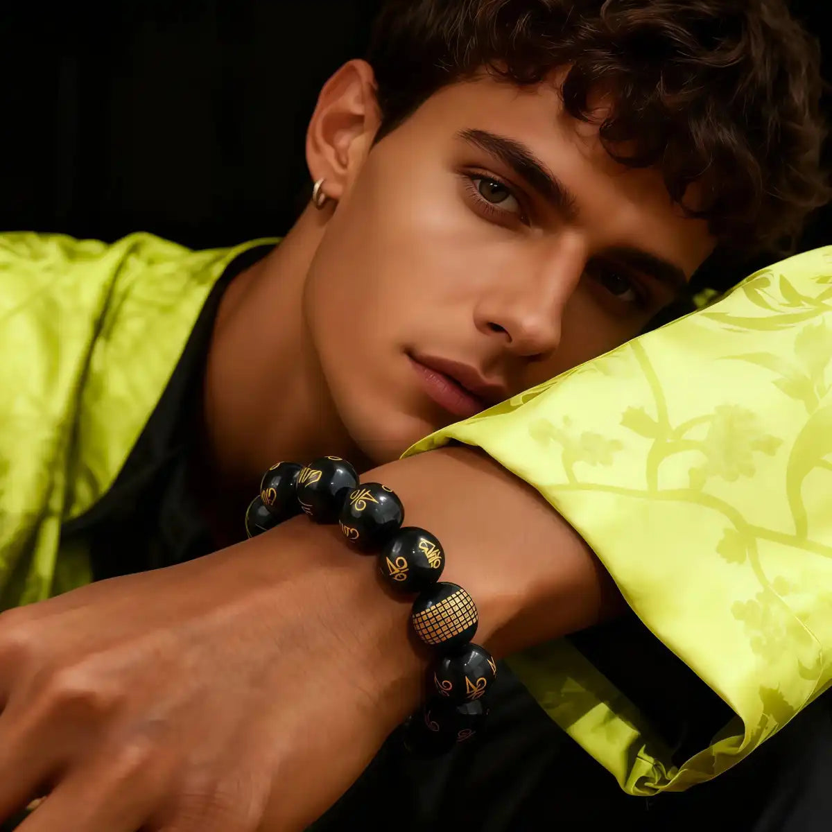 A male model in a green jacket wearing the Obsidian bracelet with gold markings.