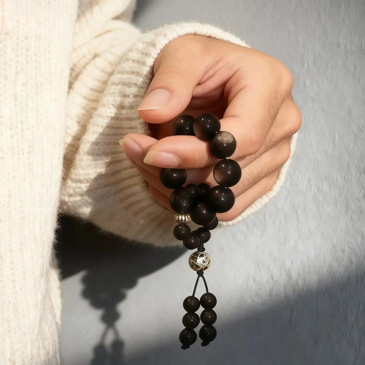 A hand holding the Black Obsidian beaded spinner against a soft beige knitted sweater.