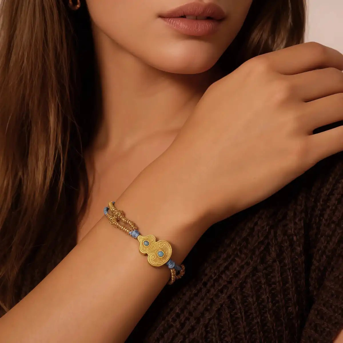 A close-up of a woman wearing the Tibetan Gourd Bracelet. The delicate blue cord and gold beads with the central gourd charm make it a stylish accessory that offers protection and attracts good fortune.