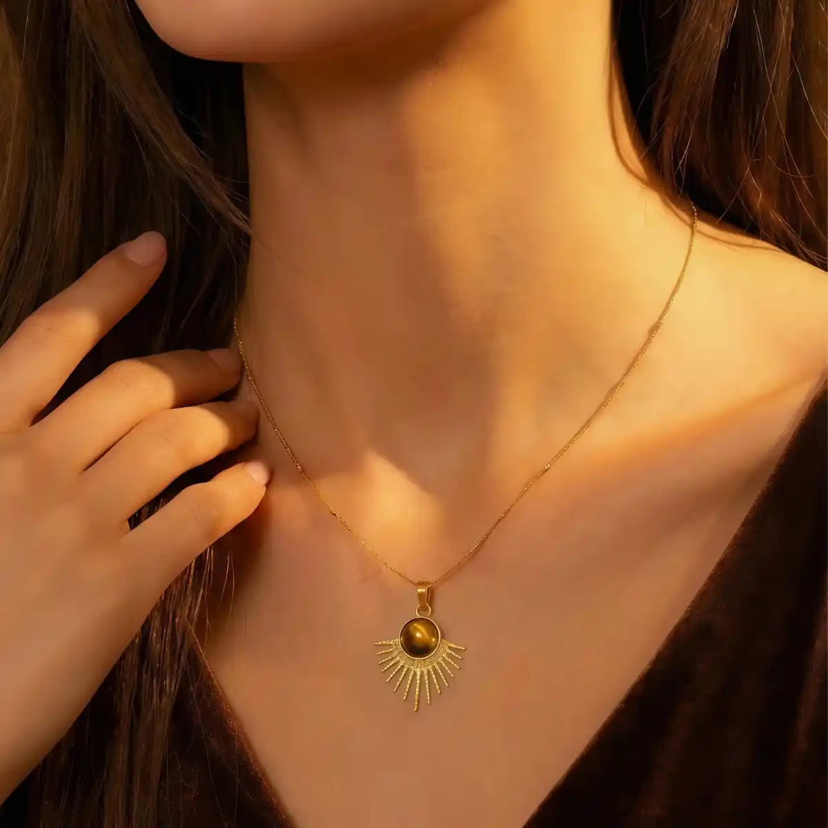 Gold necklace with a sun pendant worn by a person, with a hand adjusting the necklace.
